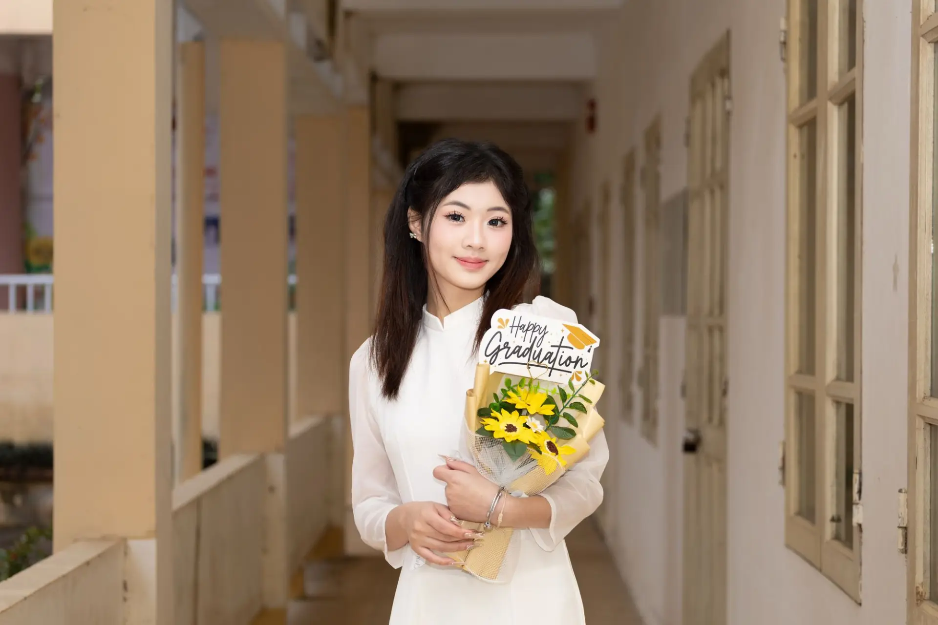 Cô gái mặc áo dài trắng cầm hoa và biển 'Happy Graduation'