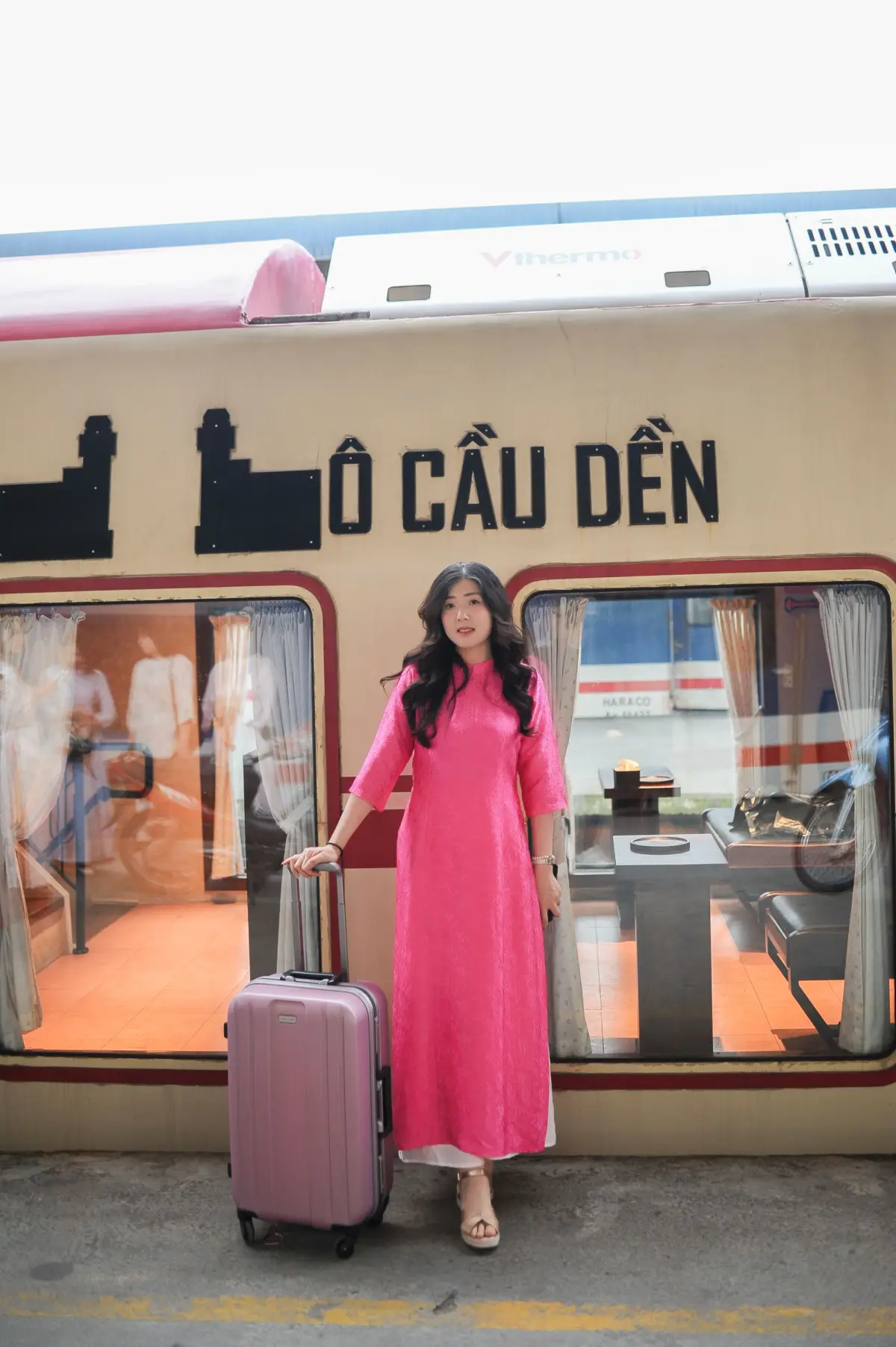 Cô gái mặc áo dài hồng kéo vali tại ga tàu